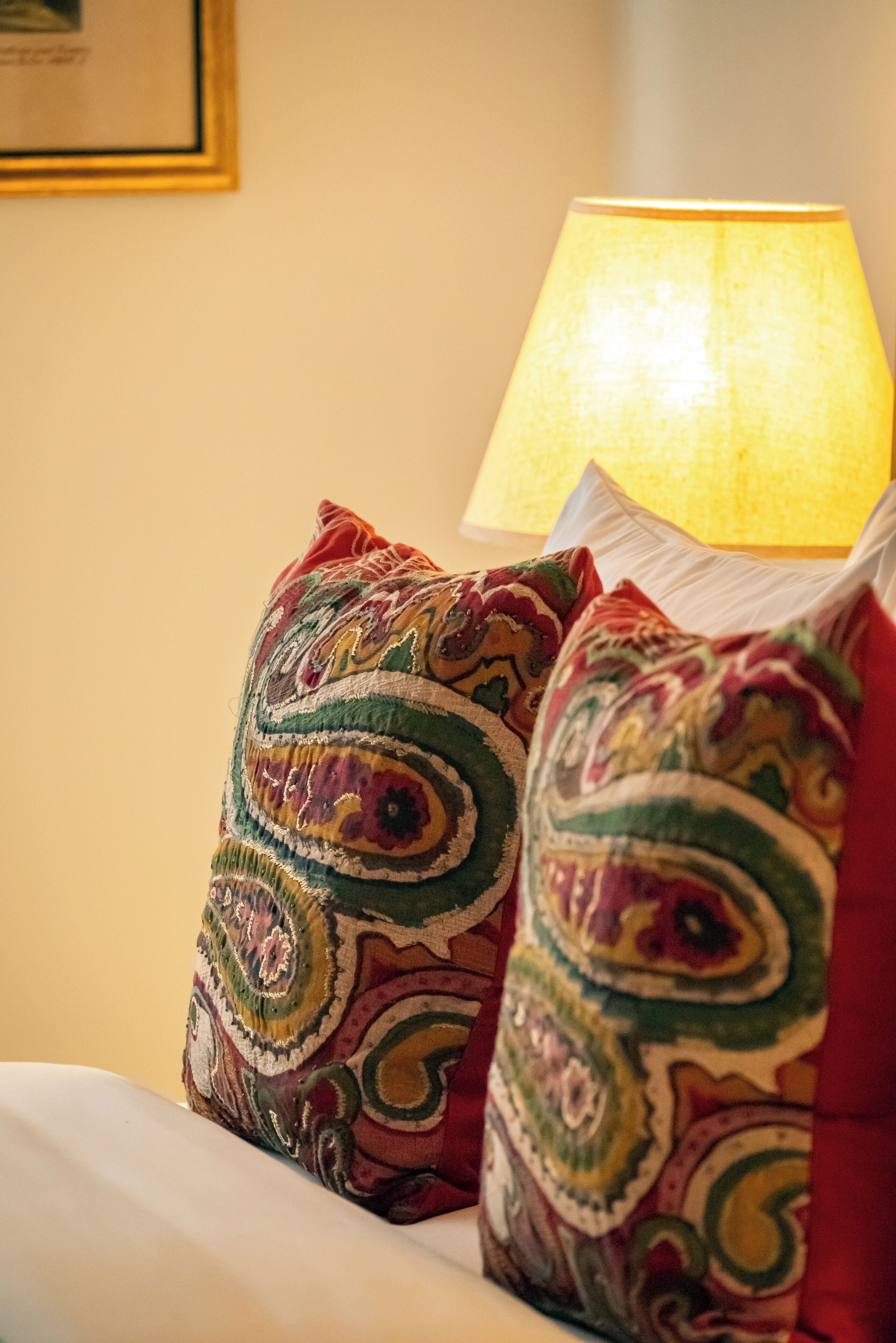 A bed with two decorative pillows and a lit table lamp.
