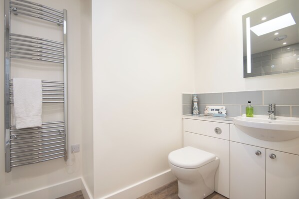 Ein Badezimmer mit chromfarbener Handtuchstange, einer weißen Toilette, einem Waschbecken mit Spiegel darüber und einem kleinen Schild am Waschbecken.