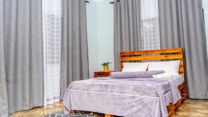 Un dormitorio con una cama de madera, cortinas grises y una mesita de noche con una planta.