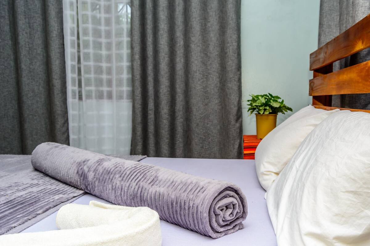 A neatly made bed with a rolled-up purple blanket, a white pillow, and a white towel on a purple bedspread.