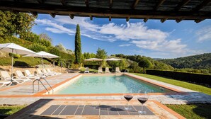 A pool area with lounge chairs and umbrellas, a table with wine glasses, and a view of the surrounding landscape. - Typical farmhouse in the heart of Chianti with private swimming pool  (Toscana)