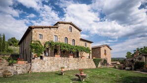 A stone building with arched windows and a covered porch, surrounded by a well-maintained garden with potted plants and a small table. - Typical farmhouse in the heart of Chianti with private swimming pool  (Toscana)