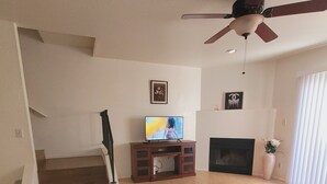 A living room with a TV on a wooden stand, a fireplace, a ceiling fan, and a staircase leading to another level. - Cozy 2-bedroom townhome in charming Tucson with AC, WiFi. Located NW of Tucson . (Tucson)
