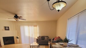 A spacious living room with a fireplace, a dining area with a table set for two, and a ceiling fan. - Cozy 2-bedroom townhome in charming Tucson with AC, WiFi. Located NW of Tucson . (Tucson)