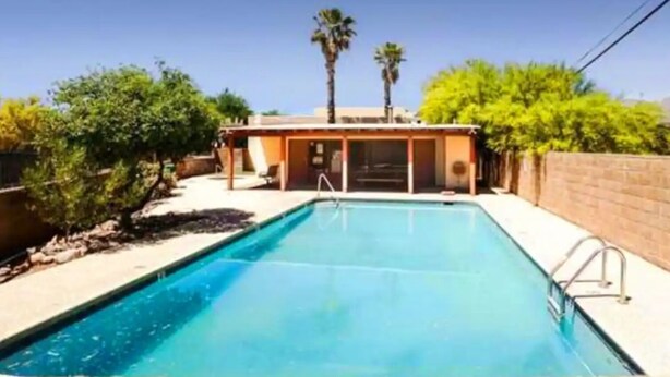 A rectangular swimming pool with a clear blue water surface, surrounded by a brick wall and a covered patio area with a door. - Cozy 2-bedroom townhome in charming Tucson with AC, WiFi. Located NW of Tucson . (Tucson)