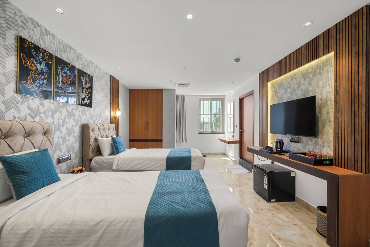 A hotel room with two beds, a TV, a desk, and a window.