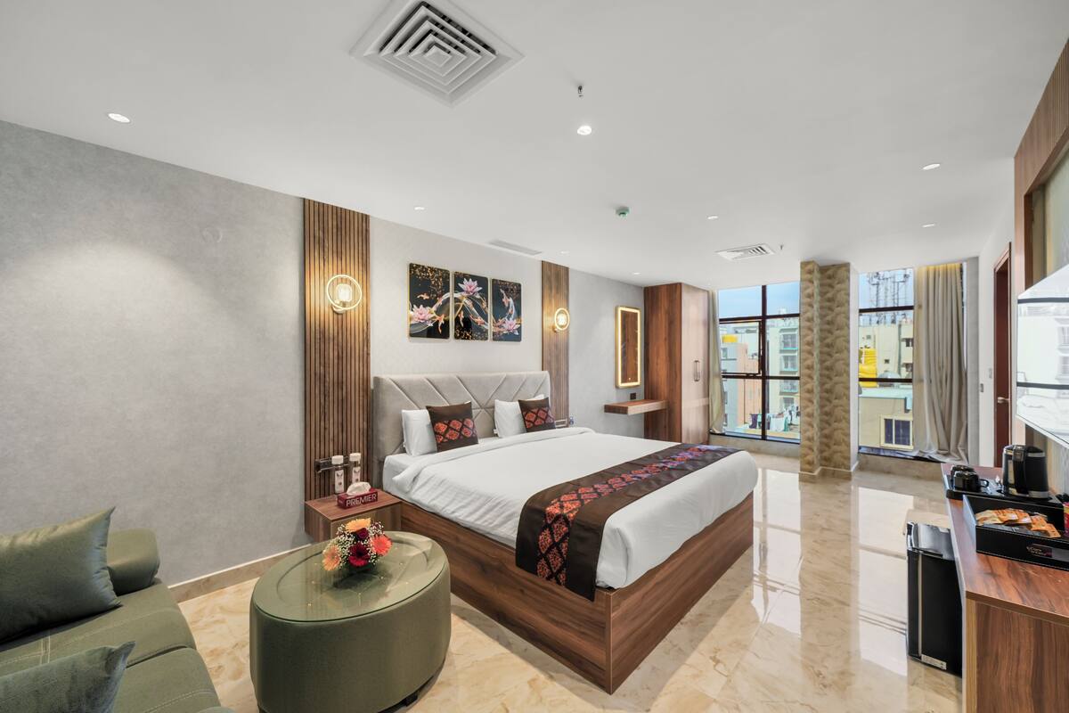 A modern hotel room with a large bed, a round coffee table, a sofa, and a view of the city.