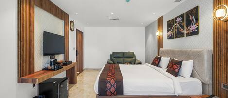 A modern hotel room with a wooden accent wall, a flat-screen TV, a sofa, a bed with patterned bedding, and artwork on the wall.