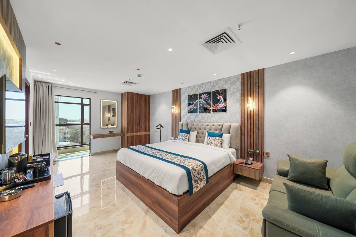 A modern bedroom with a large bed, a wooden desk, a green sofa, and a city view.