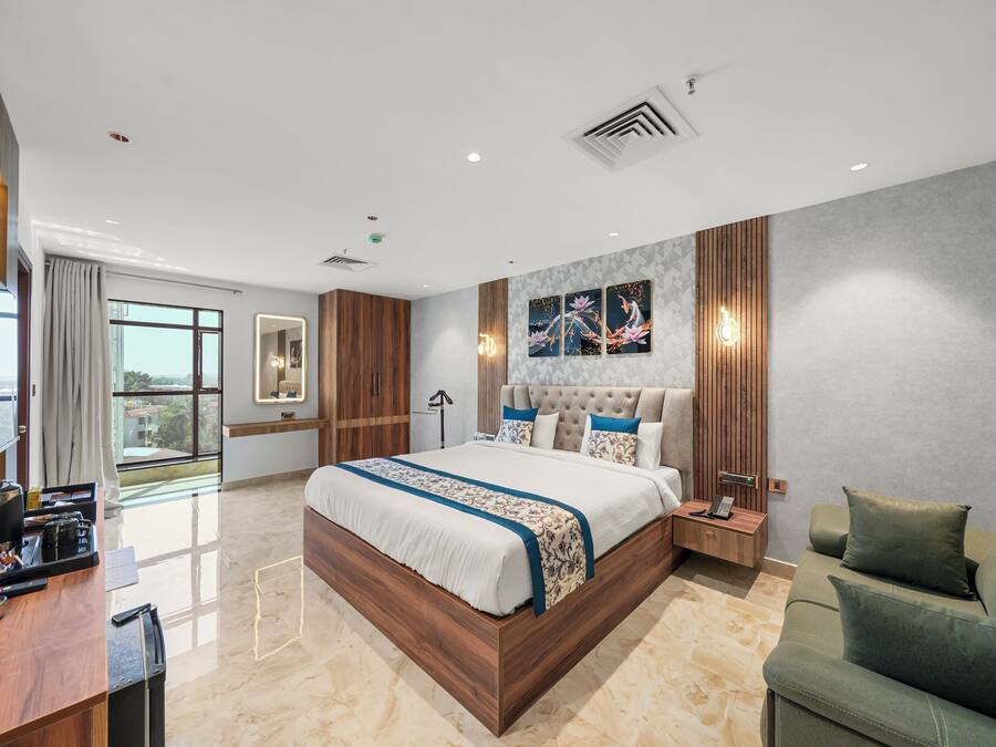 Camera da letto moderna con un letto grande, una scrivania in legno, un divano verde e vista sulla città.