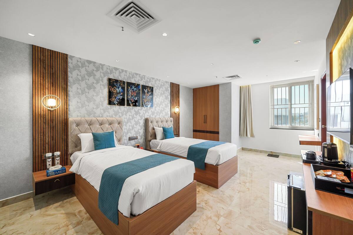 A modern hotel room with two beds, a wooden headboard, a minibar, and a large window.