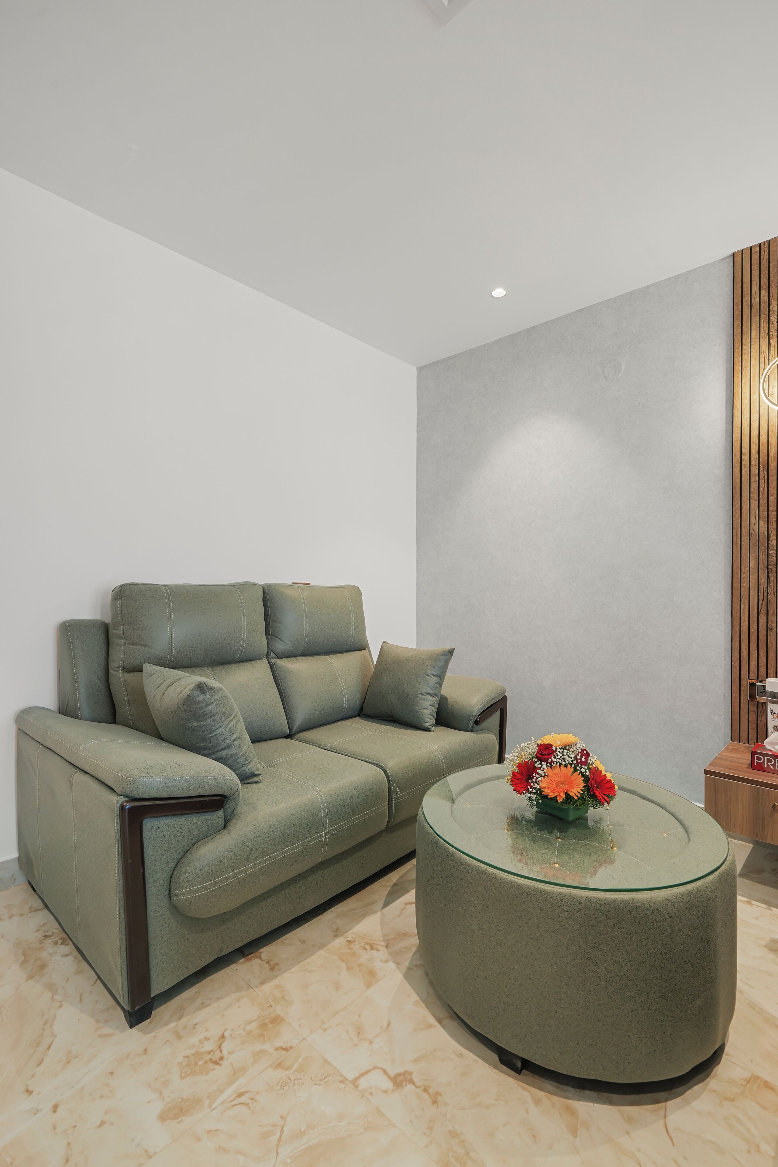 A modern living room with a green sofa, a glass coffee table, and a wooden accent wall.