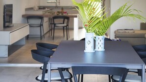 Ein moderner Essbereich mit dunklem Tisch und Stühlen, einem Blumentopf und einer Küche im Hintergrund.