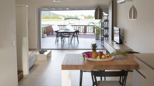 Eine moderne Küche mit Essbereich, inklusive einem Holztisch mit Obstschale, einem Fernseher und einem Balkon mit Sitzgelegenheit.