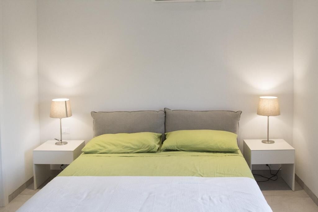 Ein ordentlich eingerichtetes Schlafzimmer mit einem Bett, zwei Nachttischlampen und einer grün-weißen Tagesdecke.