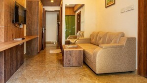 A modern living room with a sofa, a coffee table, and a TV mounted on a wooden wall. - Hotel VKJ Inn (Aluva)