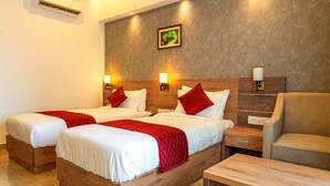 A hotel room with two wooden beds, each with white bedding and red accents, a wooden nightstand, a beige armchair, and a small table. - Hotel VKJ Inn (Aluva)