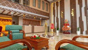 A hotel lobby with a reception desk, green upholstered seating, a decorative statue, and a marble floor. - Hotel VKJ Inn (Aluva)