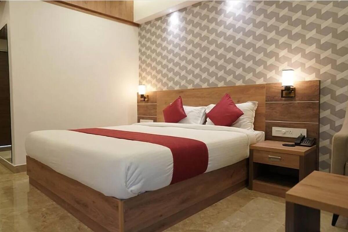 A hotel room with a large bed, wooden headboard, two bedside tables with lamps, and a small desk.