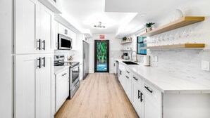 Una cocina moderna con armarios blancos, piso de madera y vista a un jardín tropical a través de un ventanal.