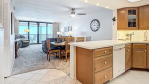 Una cocina moderna con armarios de madera, un comedor con una mesa redonda y sillas, y una sala de estar con un sofá y un balcón.