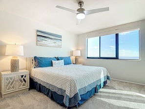 A bedroom with a bed, two bedside tables, a ceiling fan, a window, and a painting on the wall.