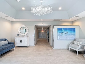 A spacious lobby with a chandelier, a large mirror, a poster, a reception desk, and a patterned sofa.