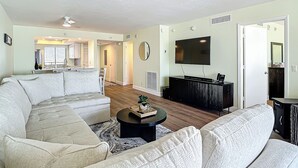 Una sala de estar con un sofá modular, una mesa de centro y un televisor de pantalla plana montado en la pared.