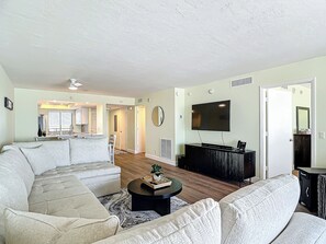 A living room with a sectional sofa, a coffee table, and a flat-screen TV mounted on the wall.