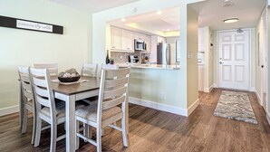 Un comedor con una mesa y sillas de madera, una cocina al fondo y un pasillo que conduce a una puerta.