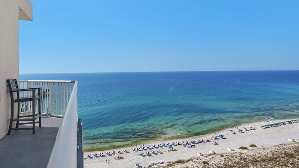 A balcony with a view of the sea, a beach with umbrellas, and a chair. - Inn At Summerwind 1405 (Navarre)
