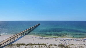A beach with a pier extending into the ocean, clear skies, and a sandy shore with umbrellas. - Inn At Summerwind 1405 (Navarre)