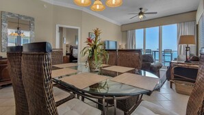 A spacious dining area with a glass table surrounded by wicker chairs, a ceiling fan, and large windows offering a view. - Inn At Summerwind 1405 (Navarre)