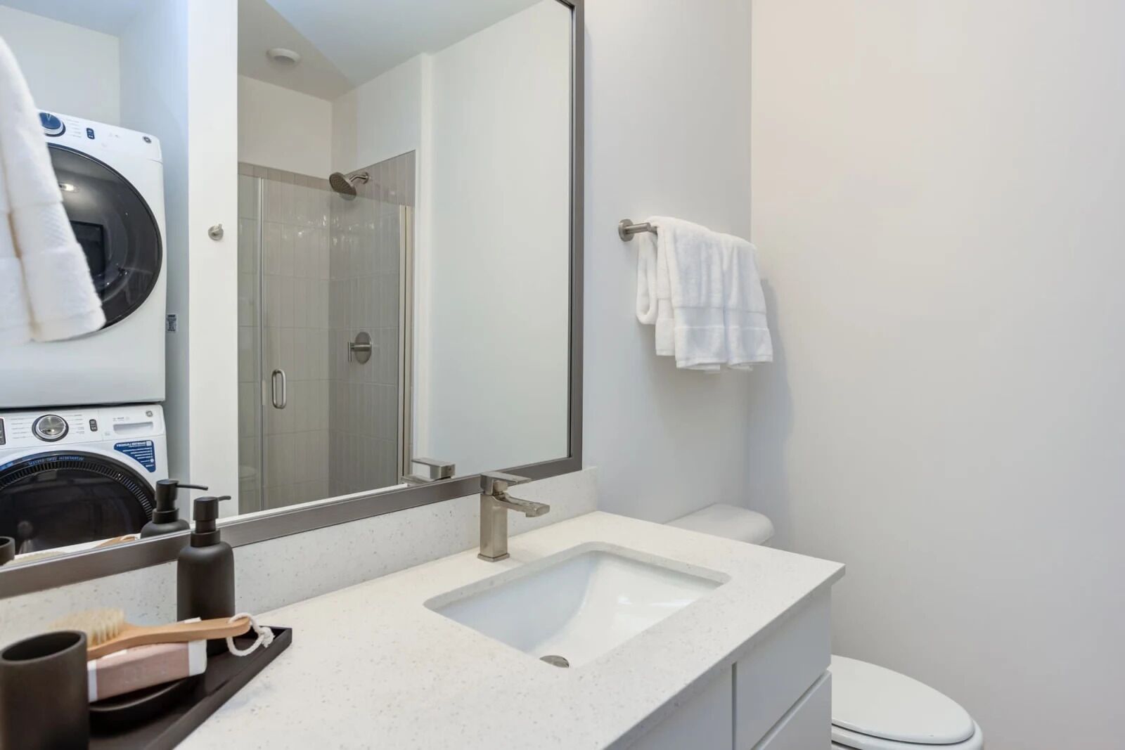 Un baño moderno con un espejo grande, dos lavamanos, un inodoro y una lavadora.