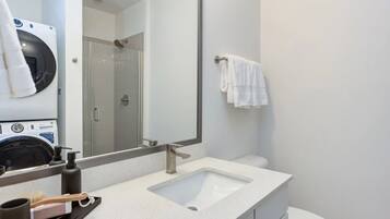 Un baño moderno con un espejo grande, dos lavamanos, un inodoro y una lavadora.