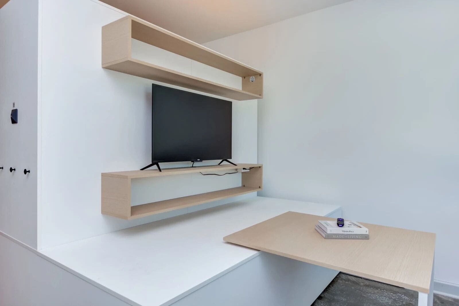 A modern, minimalist room with built-in shelving, a flat-screen TV, and a small desk with a book.