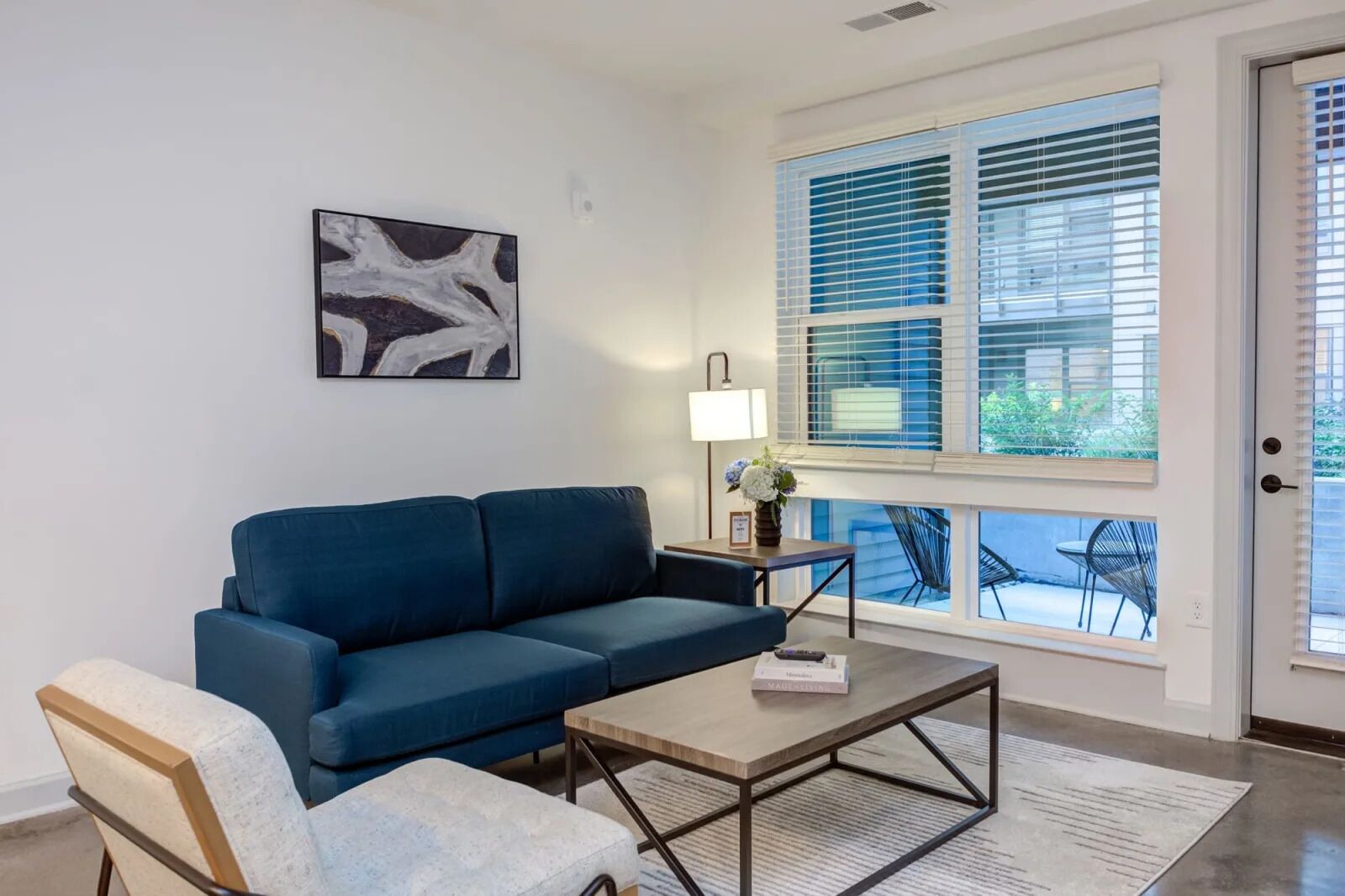 A modern living room with a blue sofa, a small table with a lamp, and a framed picture on the wall.
