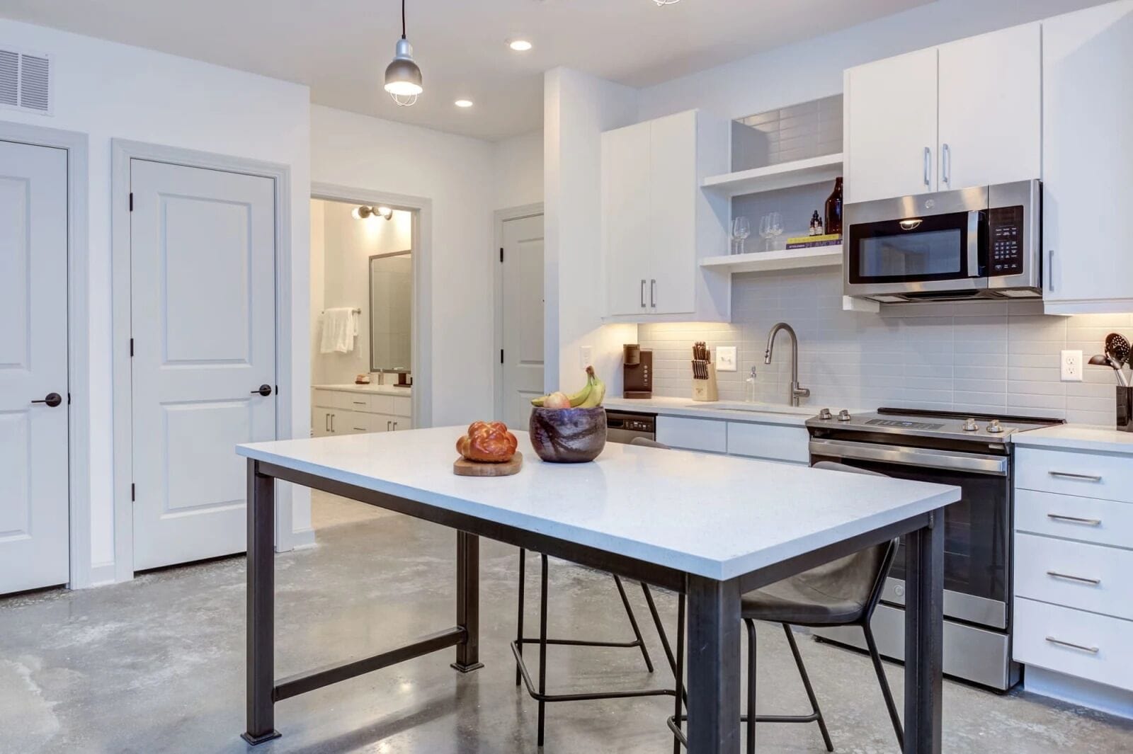 Una cocina moderna con armarios blancos, un microondas de acero inoxidable y una isla central con un bol de fruta.