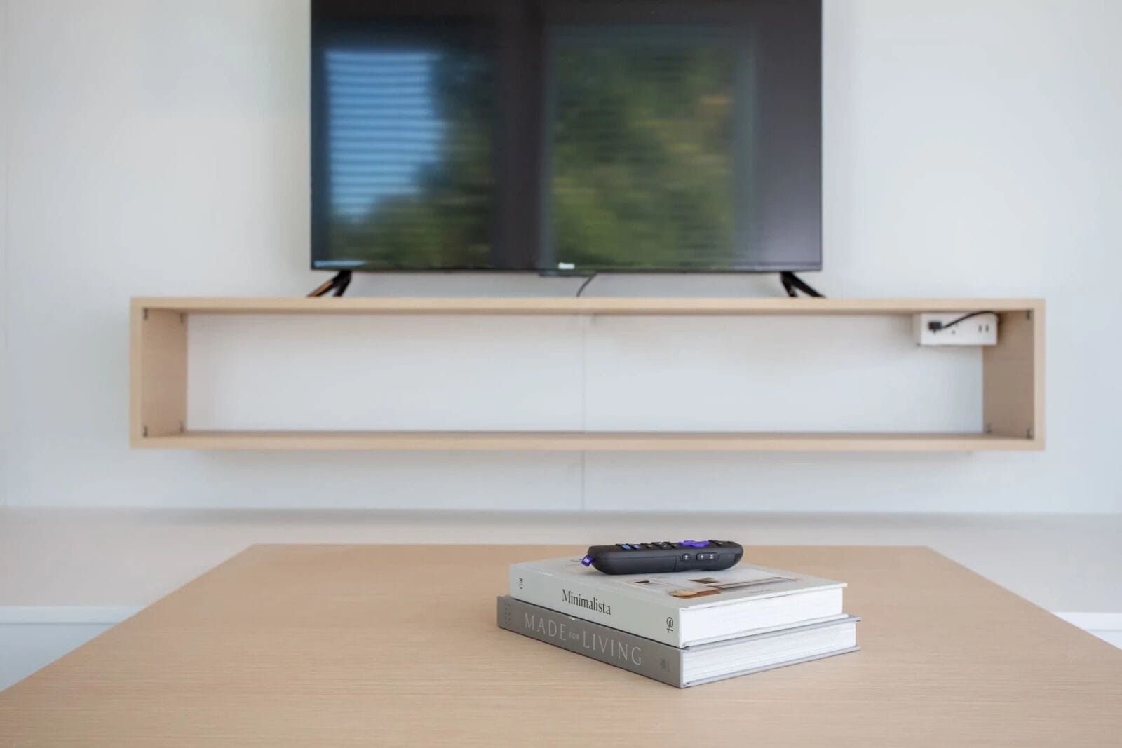 A minimalist living room with a wooden table, a remote control, and a book titled 'Minimalista MADE for LIVING'.
