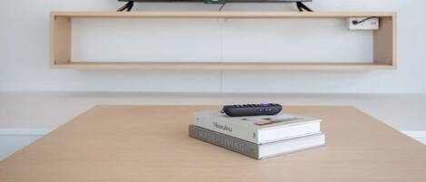 A minimalist living room with a wooden table, a remote control, and a book titled 'Minimalista MADE for LIVING'.