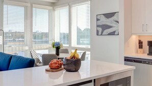Una cocina moderna con armarios blancos, una encimera blanca y vistas a la ciudad a través de amplios ventanales.
