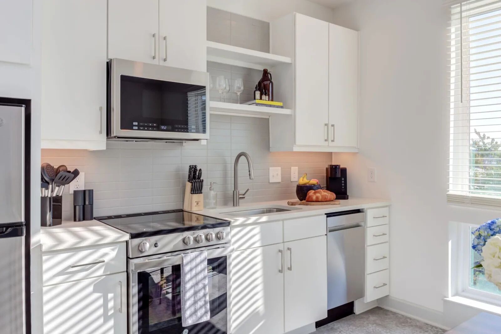 A modern kitchen with white cabinetry, a stainless steel stove, a microwave, and a dishwasher.