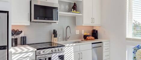 A modern kitchen with white cabinetry, a stainless steel stove, a microwave, and a dishwasher.