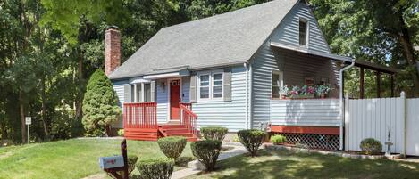 A single-story house with a red front door, a small porch, and a white picket fence.