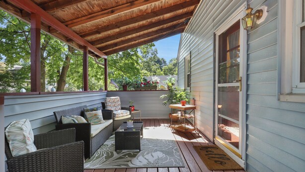 A covered porch with wicker furniture, a small table, and a doormat.