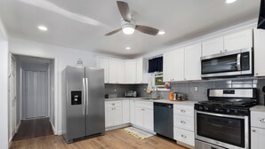 A modern kitchen with white cabinets, stainless steel appliances, a microwave, a stove, and a ceiling fan.