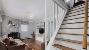 A modern living room with a staircase, wooden flooring, a sofa, a TV, and a fireplace.