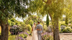 A couple walking under an archway in a garden with various plants and flowers.