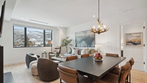 Een moderne eetruimte met een grote tafel, lederen stoelen en een kroonluchter.