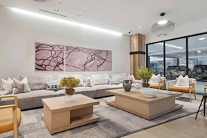 Un salon moderne avec un canapé gris, deux tables basses en bois et un grand tableau abstrait accroché au mur.